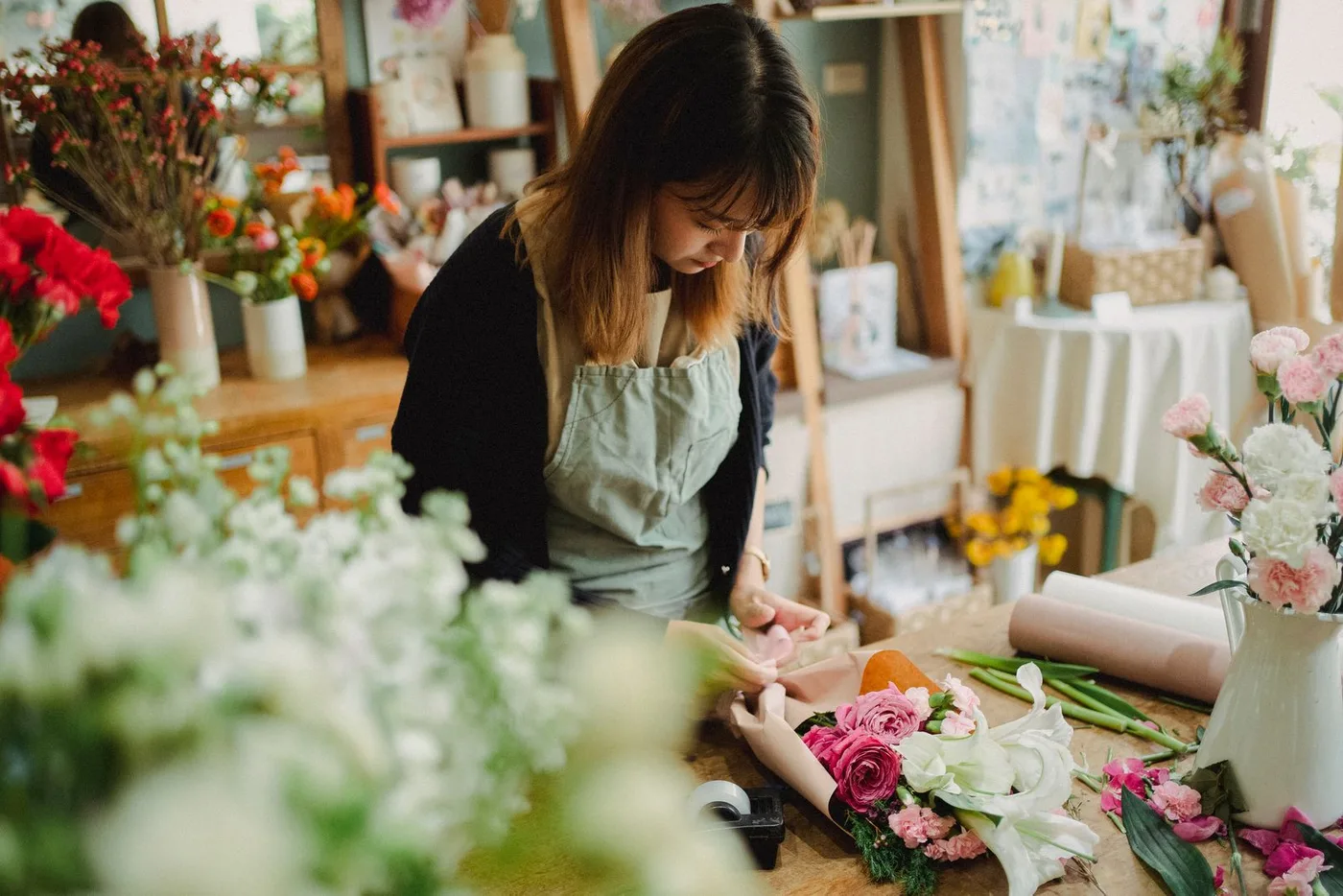 Une fleuriste compose un bouquet dans sa boutique entourée de fleurs et de présentoirs